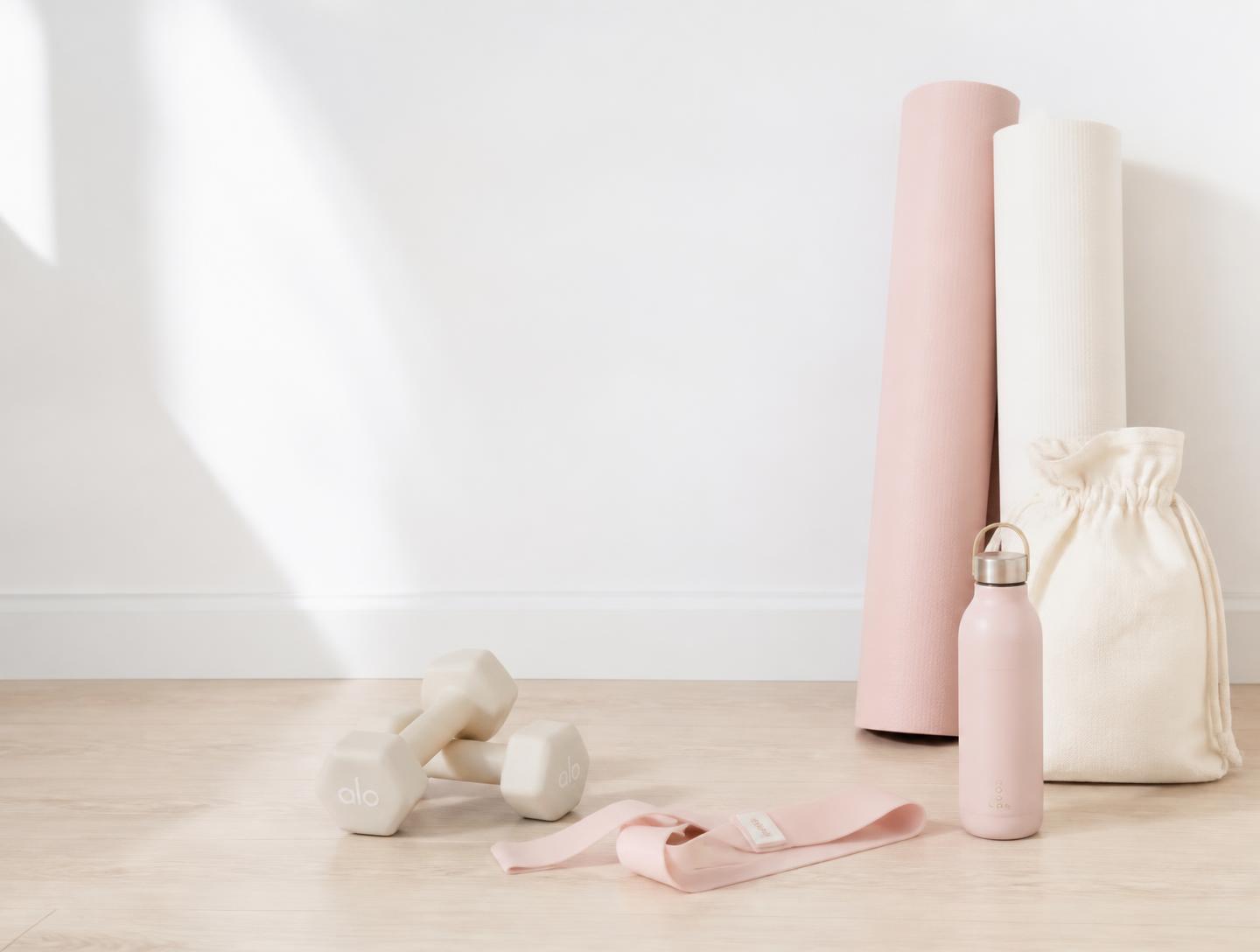 Rolled mats, light dumbbells and a resistance band against a white wall in soft daylight