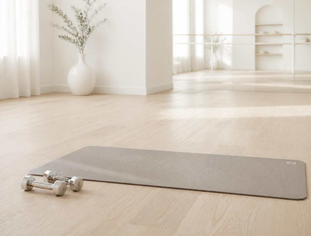 Light chrome hand weights beside a mat on pale oak flooring in a bright white studio